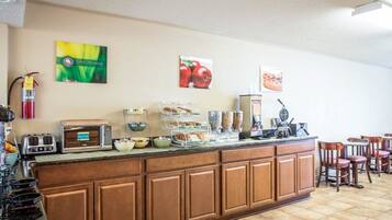 Una barra de desayuno con diversas opciones de alimentos y una máquina de café. Hay sillas y un extintor en la pared.