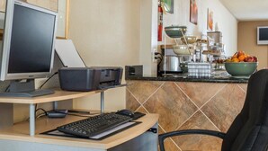 A hotel room with a desk, computer, and chair. There is a kitchen area with a stove, sink, and countertop. - Quality Inn & Suites Monroe (Monroe)