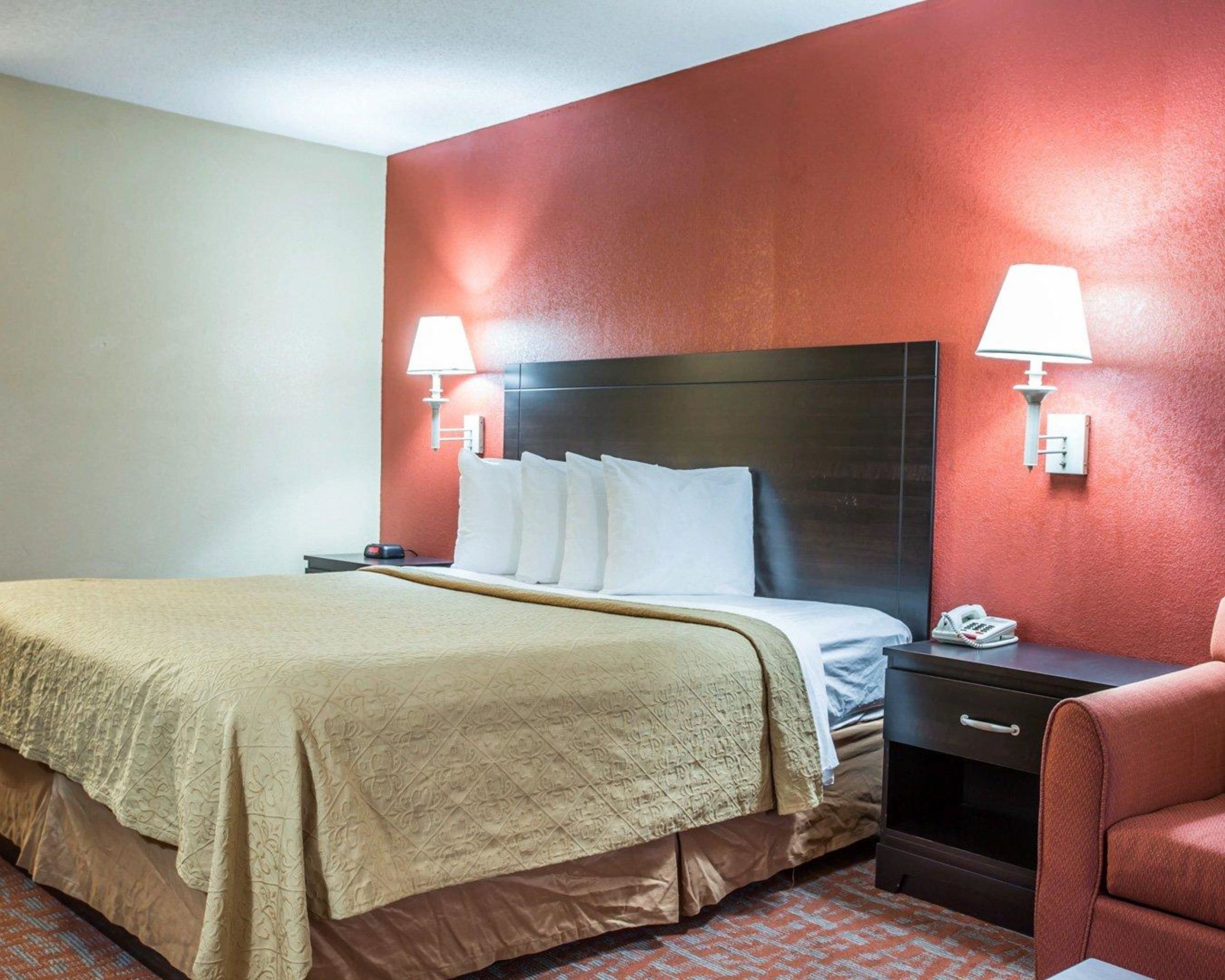 A hotel room with a large bed, two bedside tables, a nightstand, a chair, and two wall-mounted lamps.