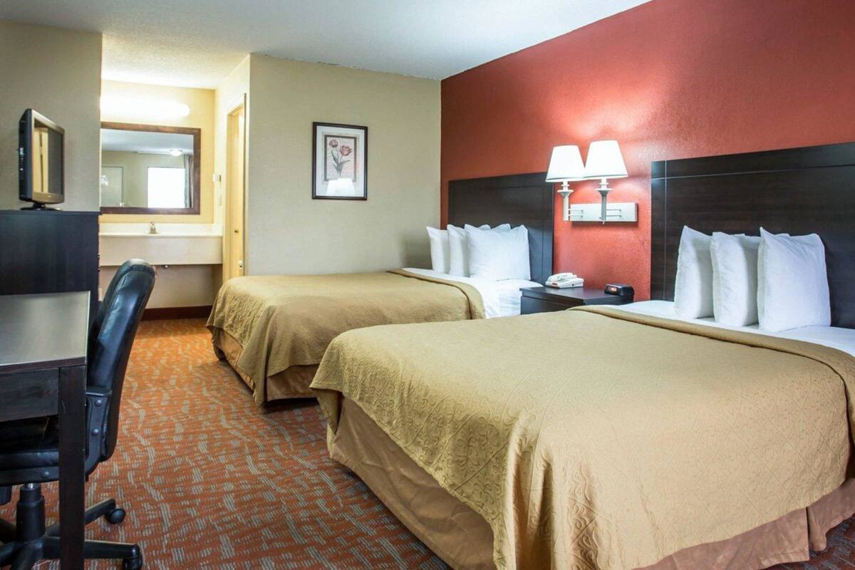 Quarto de hotel com duas camas, uma mesa, uma cadeira, uma televisão, um espelho e um quadro na parede.