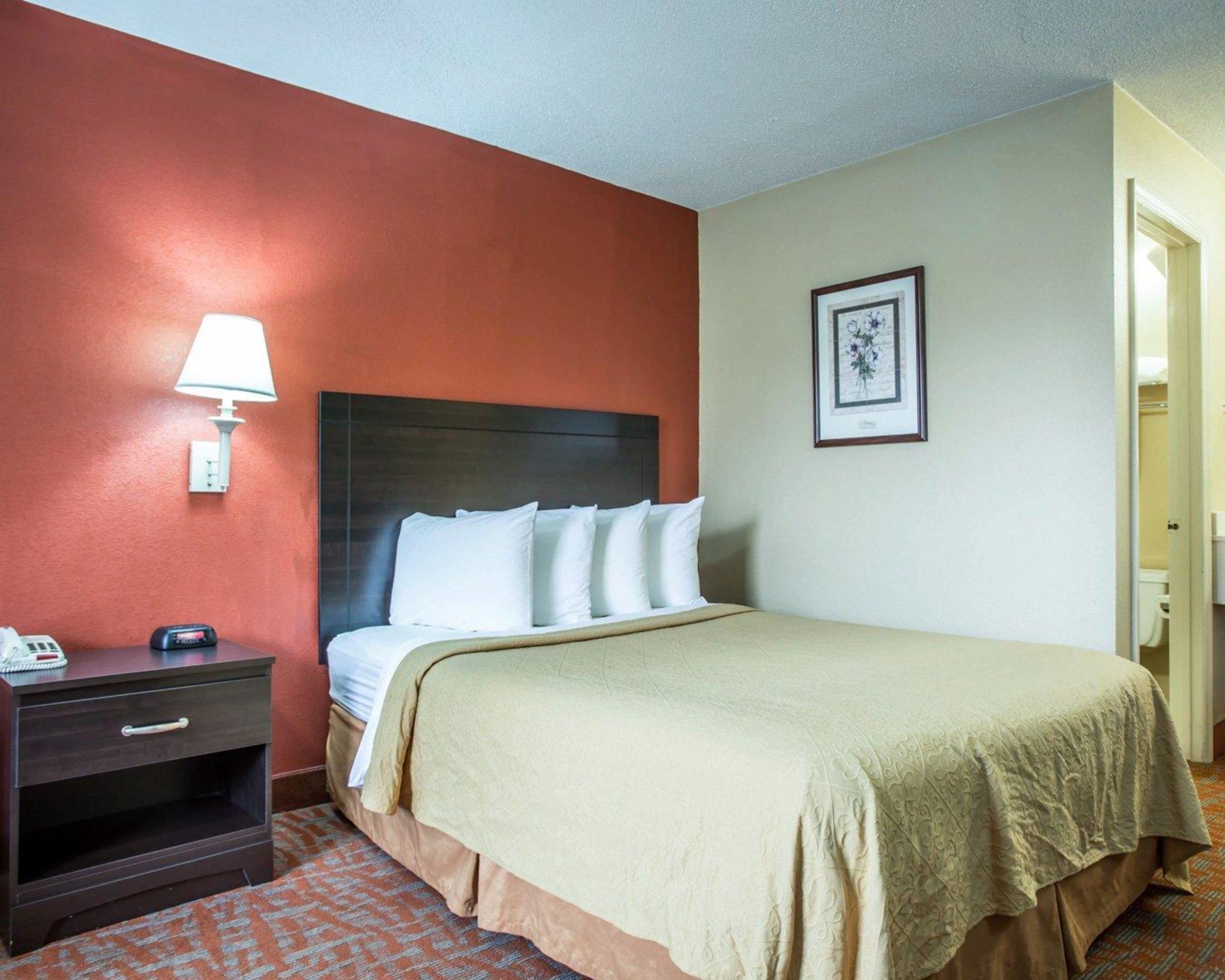 Una habitación de hotel con una cama, una mesita de noche, una lámpara y un cuadro en la pared.