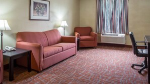 A hotel room with a sofa, armchair, desk, and air conditioning unit. - Quality Inn & Suites Monroe (Monroe)
