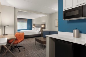 Une chambre d’hôtel comprenant un lit, un bureau, une chaise, un coin cuisine et un mur d’accent bleu.