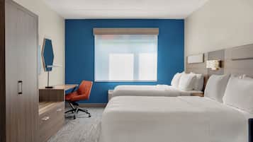 A hotel room with two beds, a desk, a chair, and a large window with blinds.