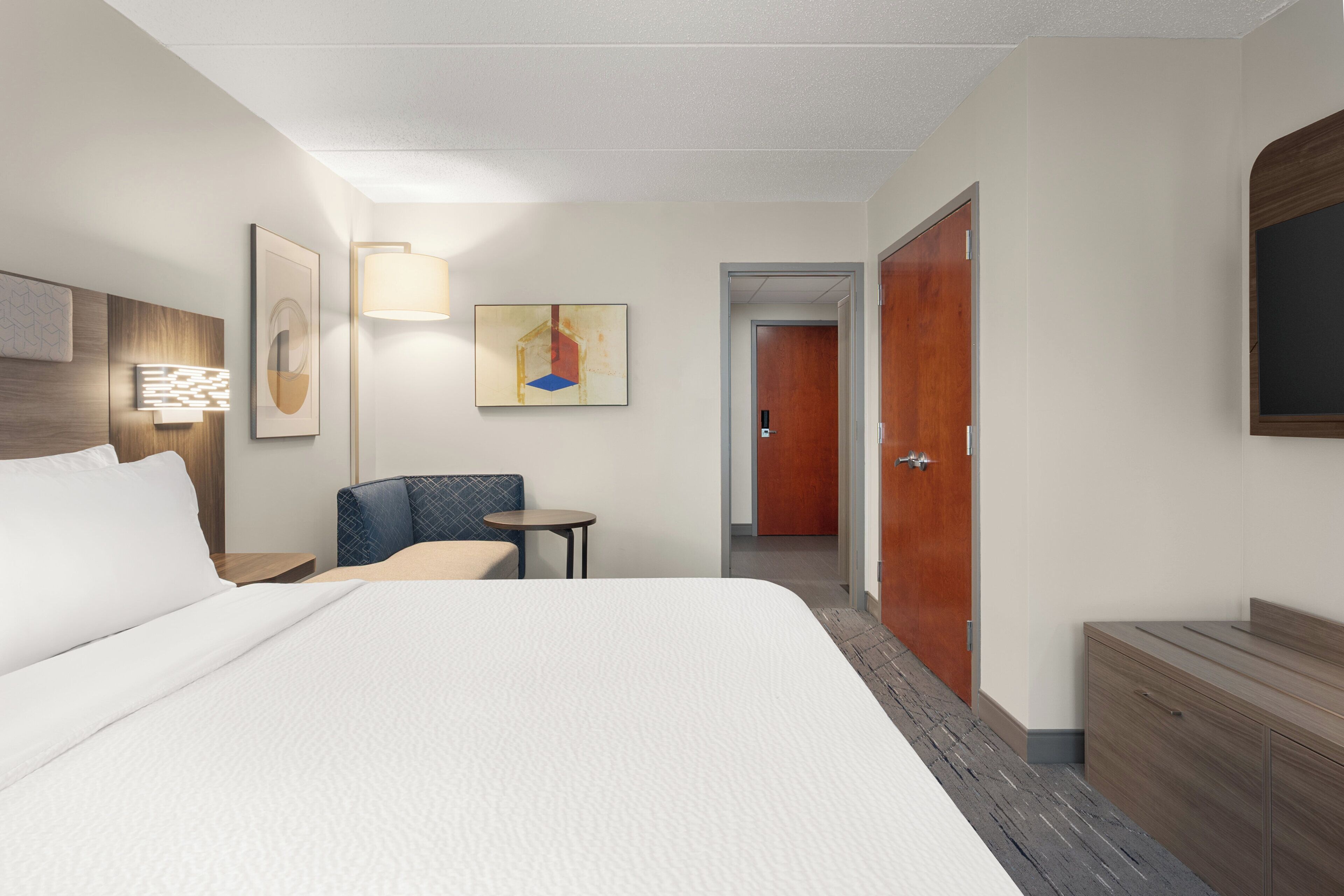 Et hotelværelse med en stor seng, et skrivebord, en stol, et lille bord og en garderobe.