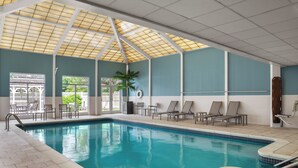 En indendørs swimmingpool med fliset gulv, loft med et gittermønster og udsigt til grøn bevoksning udenfor.