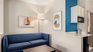 A modern hotel room with a blue sofa, a wooden coffee table, a lamp, and artwork on the walls.