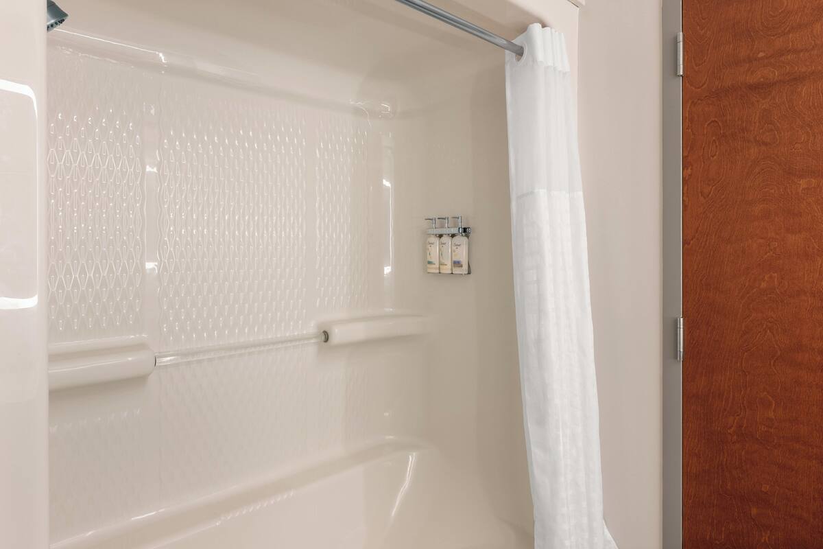 A bathroom with a shower, a wooden door, and a towel rack with bottles.