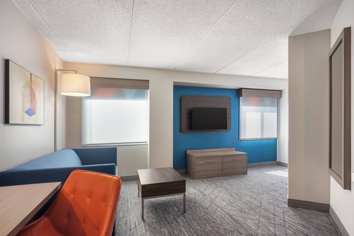 A modern office space with a blue accent wall, a mounted TV, a wooden cabinet, and a seating area with a table and chairs.