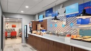 En moderne morgenmadsbar med et varieret udvalg af mad, herunder morgenmadsprodukter og varme retter. Skilte angiver, hvor man kan finde morgenmad og varme retter.