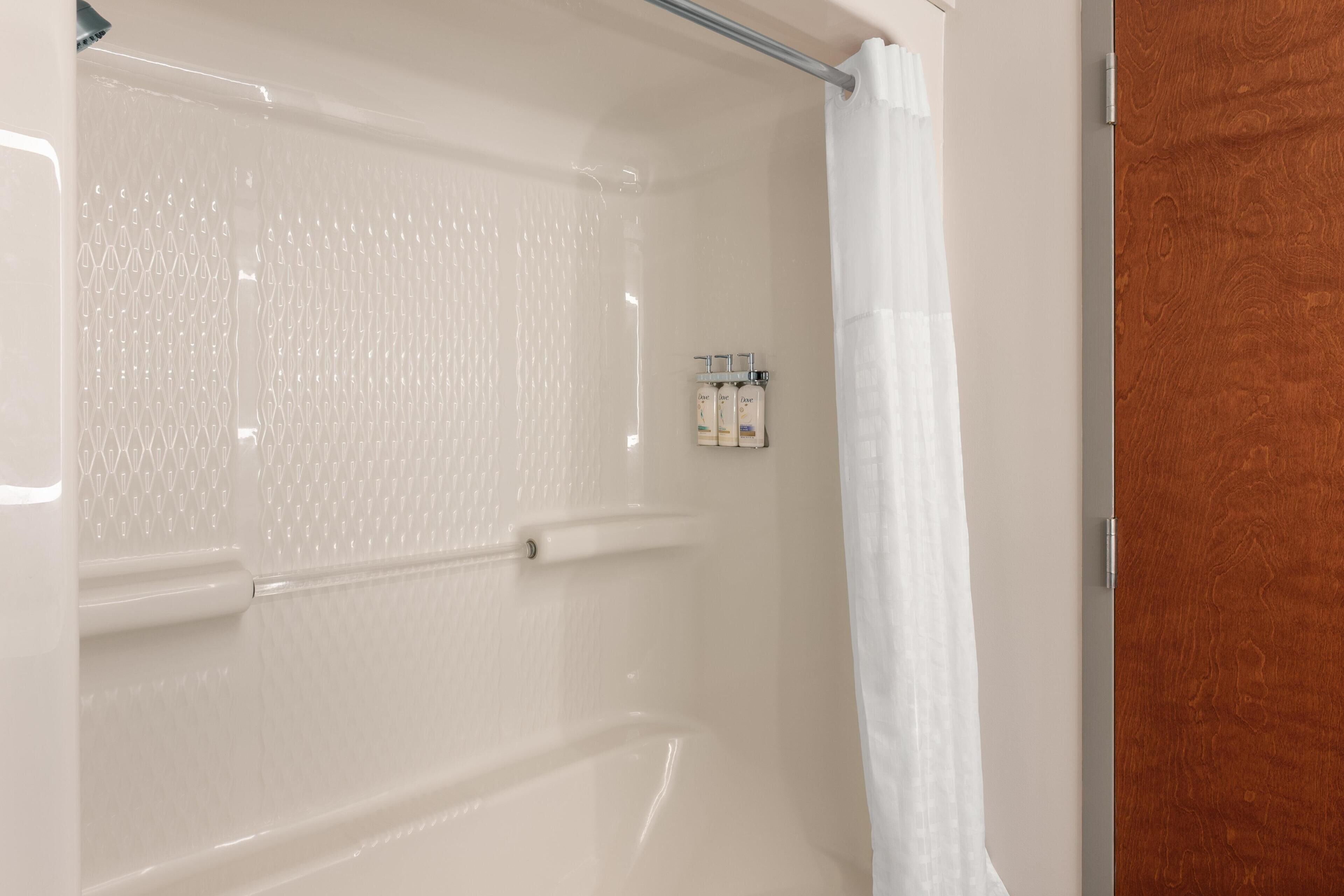 A shower area with a glass door, a white shower curtain, and a wooden door frame.