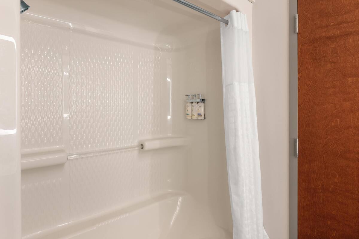 A shower area with a glass door, a white shower curtain, and a wooden door frame.
