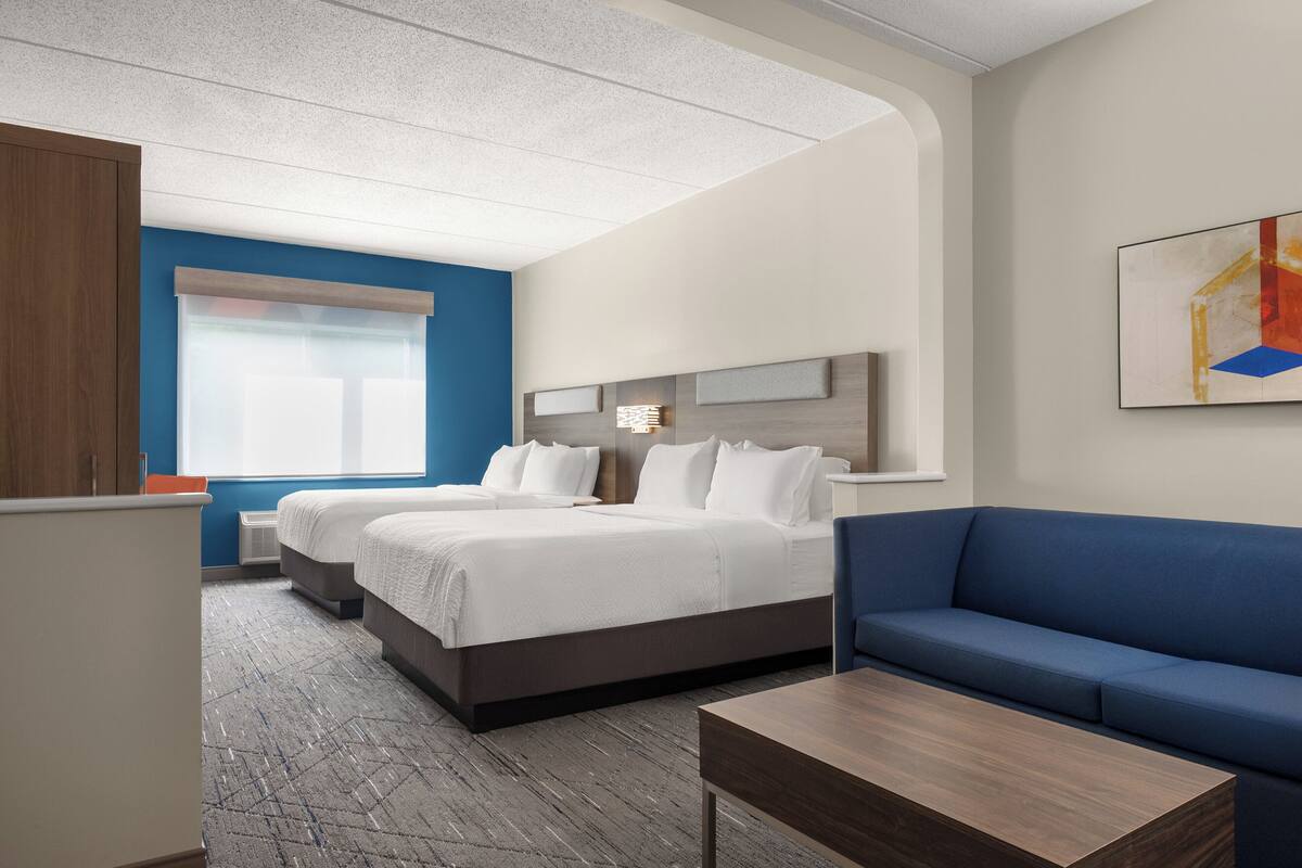 A hotel room with two beds, a blue sofa, a wooden coffee table, and a painting on the wall.