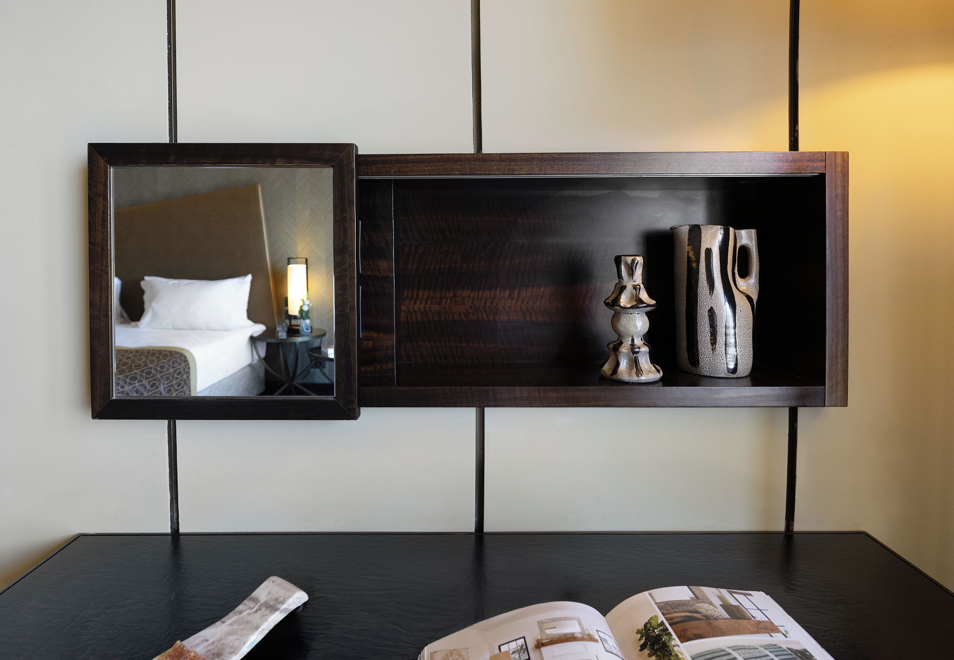 Een hotelkamer met een bed, nachtkastje, lamp en een plank met decoratieve objecten.