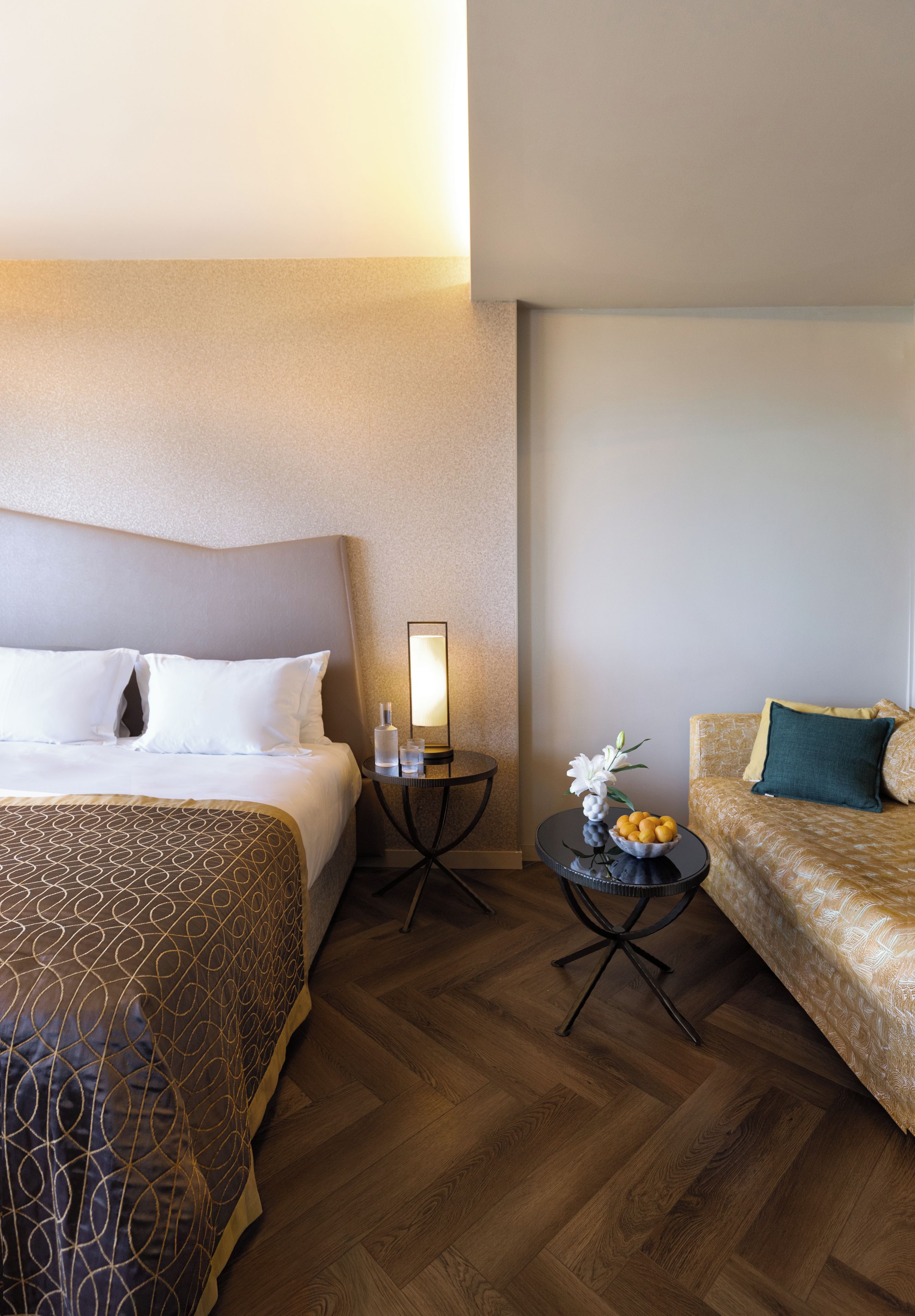 Habitación de hotel con una cama, una mesita con una lámpara, un sofá y un cuenco decorativo en el suelo.