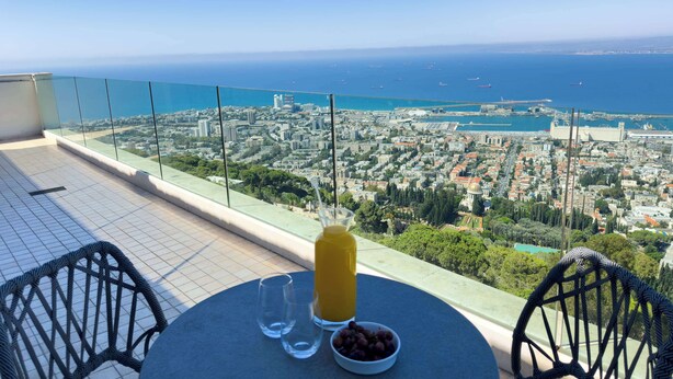 A balcony with a table, two chairs, a glass of water, a tall glass of juice, and a bowl of grapes. - The Dan Carmel Hotel (Haifa)