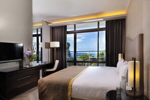 Una habitación de hotel con una cama, un escritorio, un televisor y vista al mar.