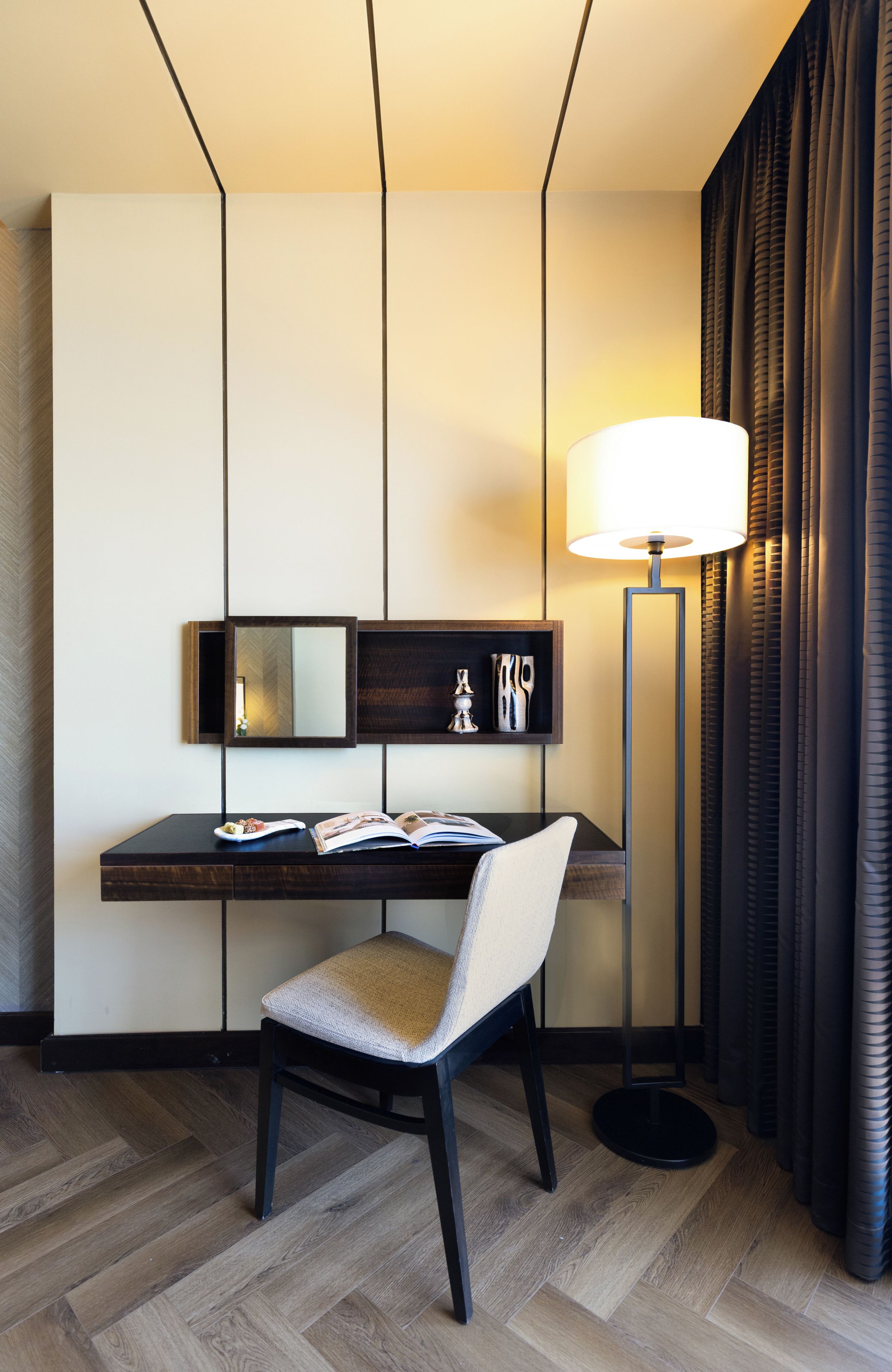 Una habitación de hotel con escritorio, silla, lámpara y cortinas.