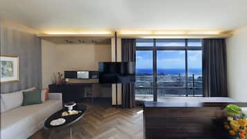A modern living room with a sofa, coffee table, TV, and a view of the city through large windows.