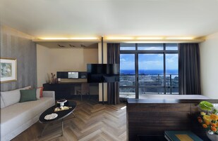Ein modernes Wohnzimmer mit Sofa, Couchtisch, Fernseher und Blick auf die Stadt durch große Fenster.