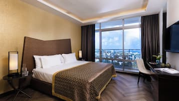 Habitación de hotel con una cama grande, un escritorio con silla, un televisor y vistas a un paisaje urbano a través de un ventanal amplio.