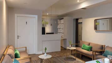 A modern living room with a sofa, chairs, a small table, and a coffee table. There is a door, a mirror, and a window with curtains.