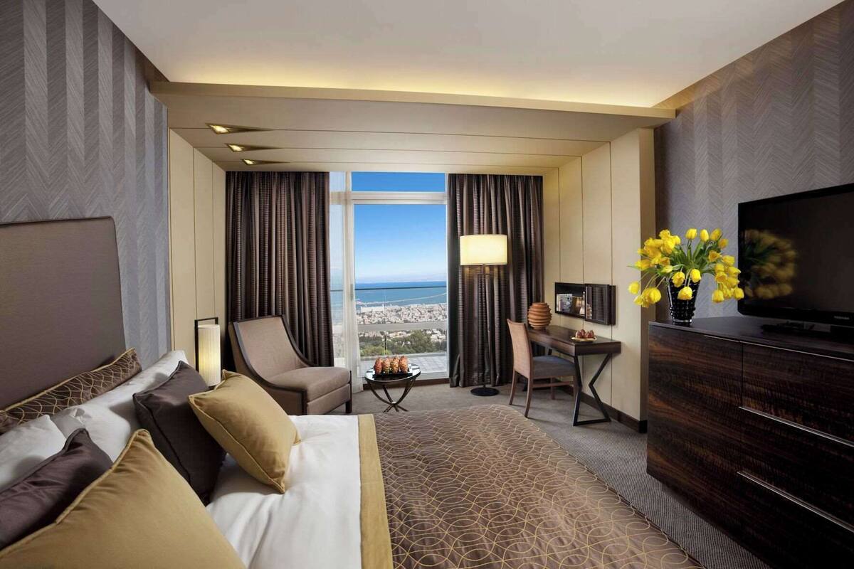 A hotel room with a bed, a desk, a chair, a TV, and a view of the city.
