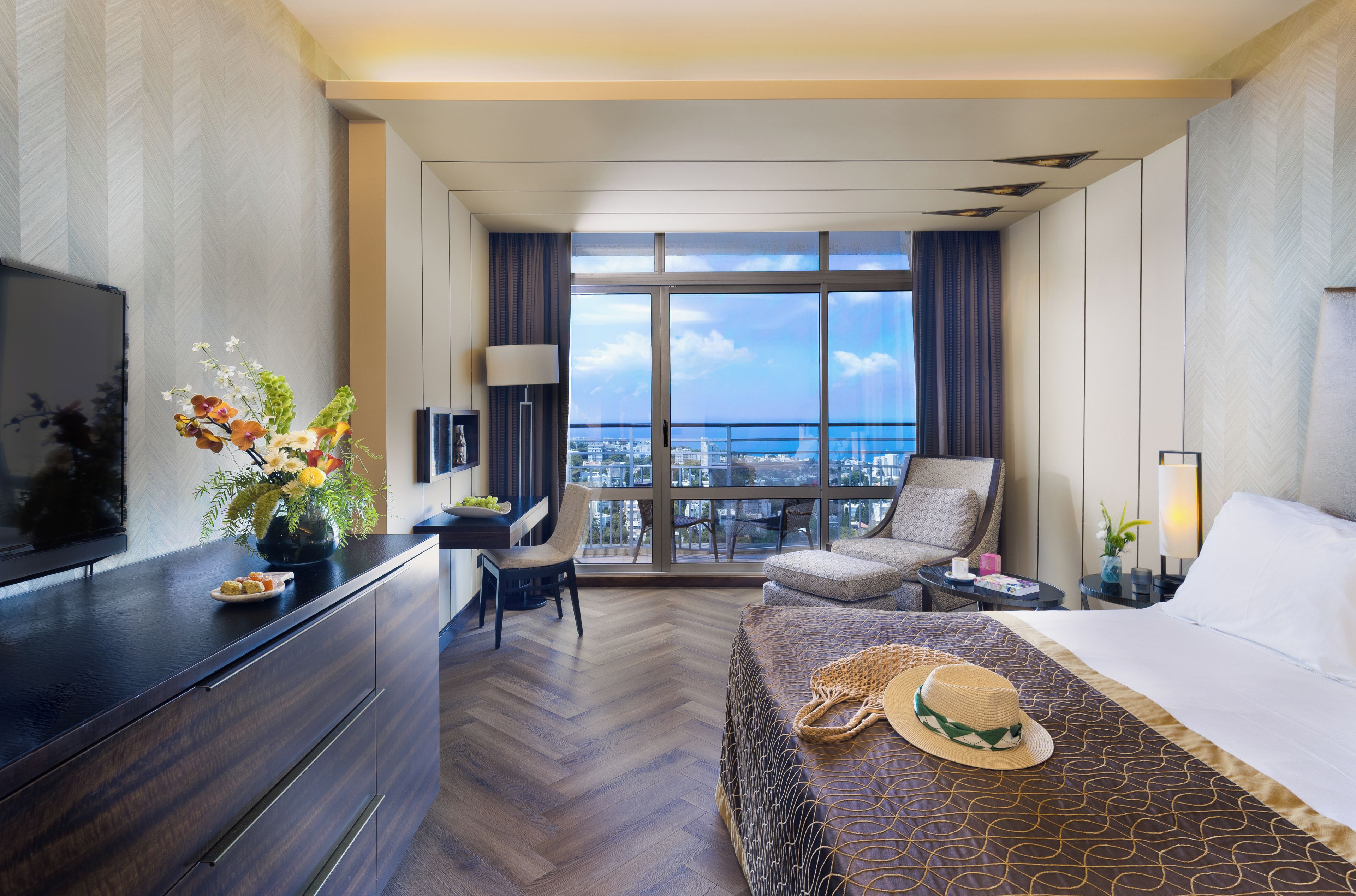 Habitación de hotel con un ventanal grande, una cama, un televisor, un escritorio y una silla.