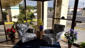 A covered outdoor seating area with two patterned armchairs, a blue rug, and potted plants. - Western Inn (Pensacola)