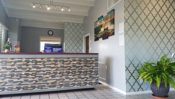 A reception area with a stone-patterned counter, a clock, and a large painting on the wall. - Western Inn (Pensacola)