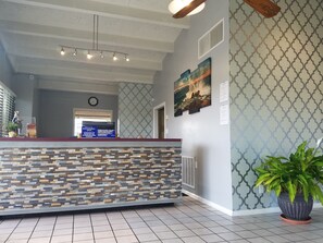 A reception area with a stone-patterned counter, a clock, and a large painting on the wall. - Western Inn (Pensacola)