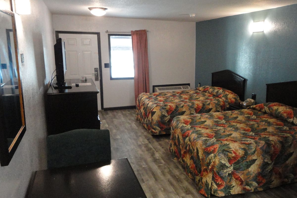 A hotel room with two beds, a desk, a chair, a mirror, and a window with curtains.
