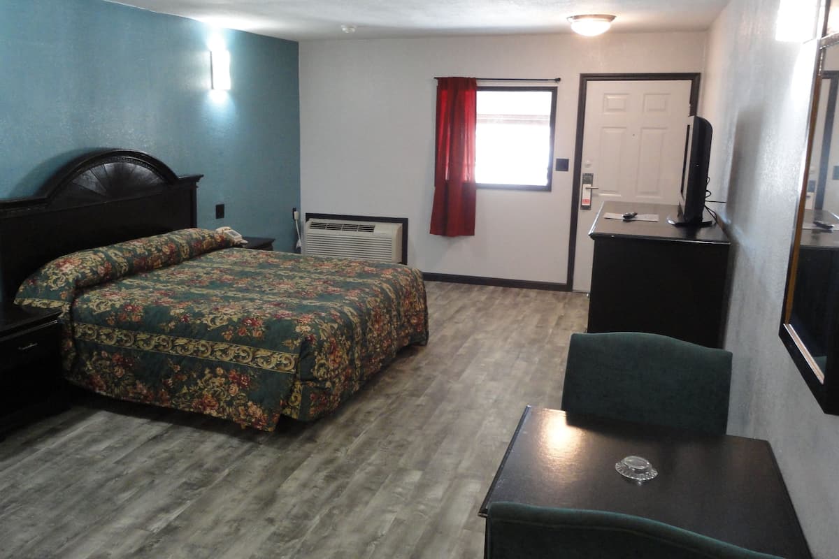 A hotel room with a bed, a desk, a chair, a TV, and a window with curtains.