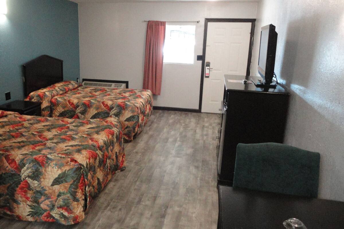 A hotel room with two beds, a desk, a chair, a television, and a door.
