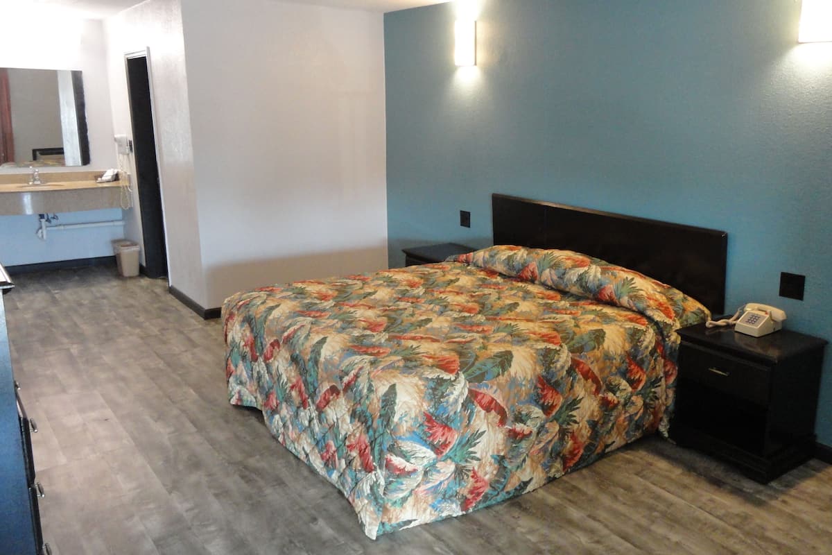 A bedroom with a floral bedspread, a nightstand with a phone, and a mirror above the dresser.
