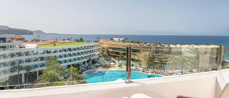 A hotel balcony with a pool, overlooking a coastal area with buildings and a clear sky.