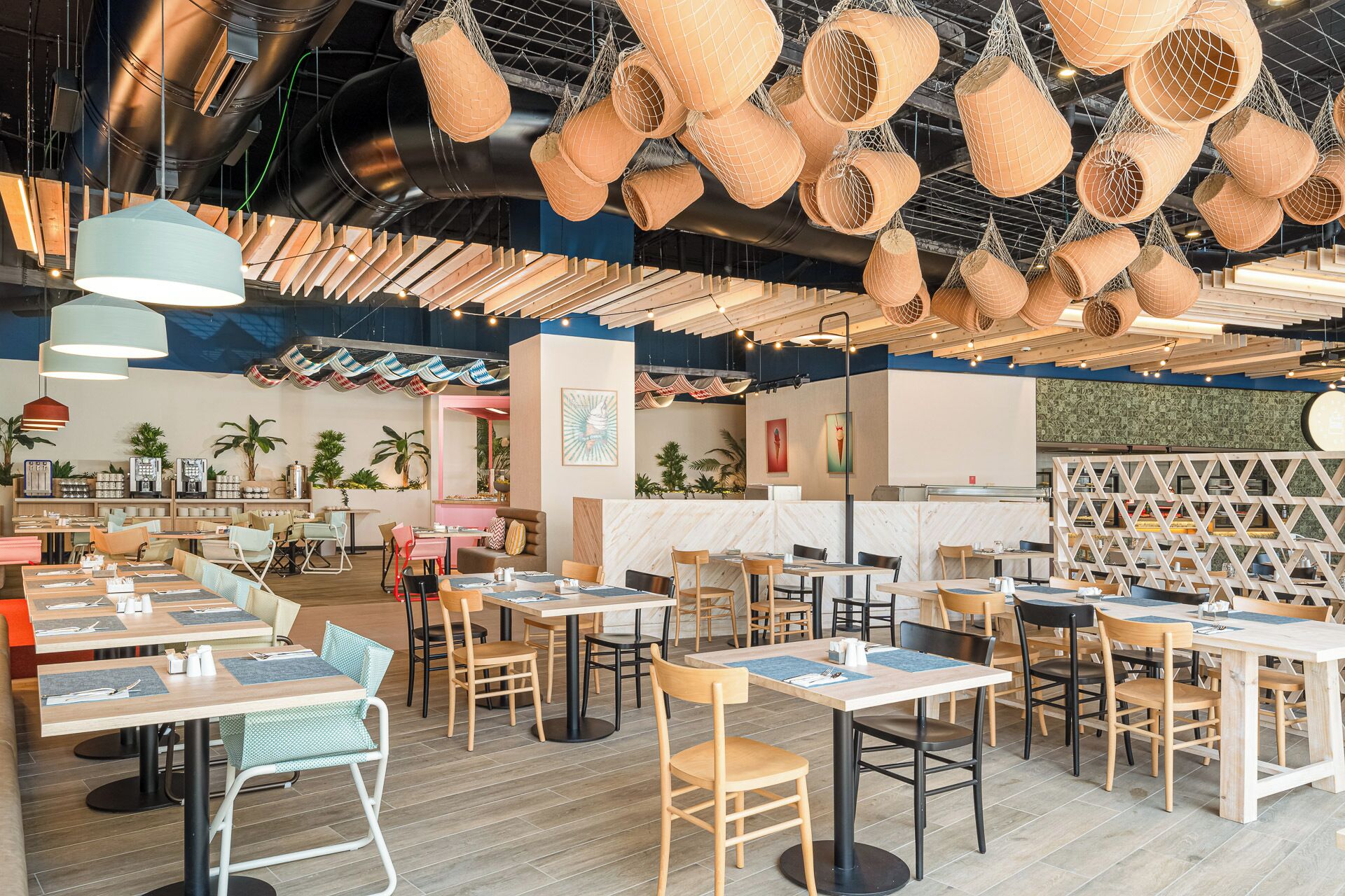 Ein modernes Restaurant mit mehreren Tischen und Stühlen, hängenden Körben und verschiedenen Pflanzen.