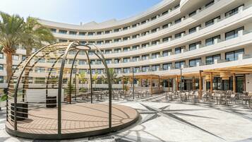 Um hotel com área de estar circular ao ar livre, uma escultura central e um edifício moderno de vários andares com varandas.