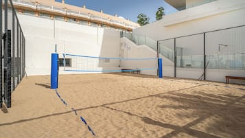 Een strandvolleybalveld met een net, banken en een trap naar een gebouw met balkons.
