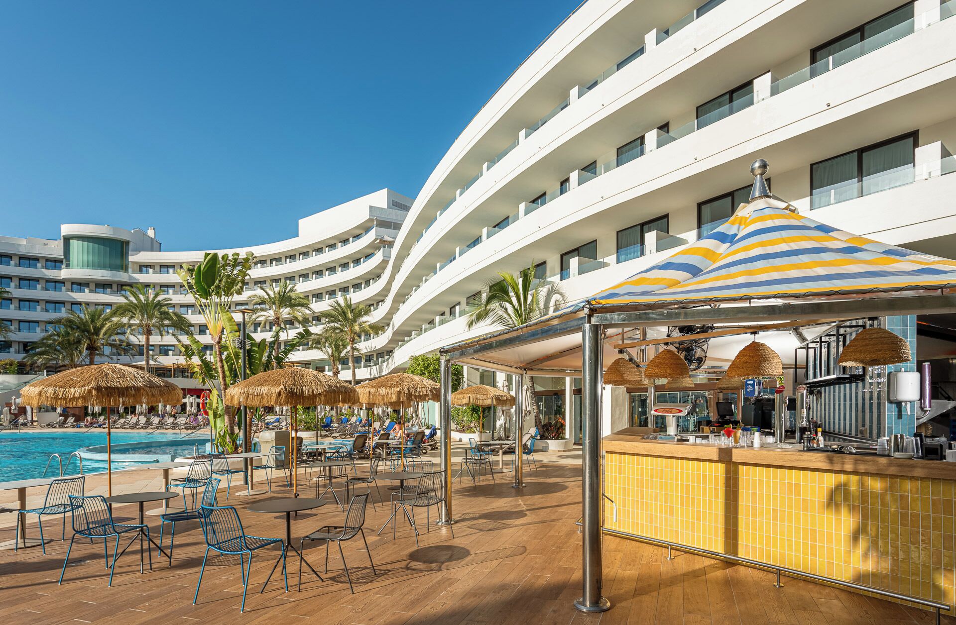 Un espace piscine aménagé dans un complexe hôtelier, avec des chaises longues, des parasols et un bar.