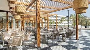 An outdoor cafe area with wicker furniture, a checkered floor, and a wooden pergola structure.