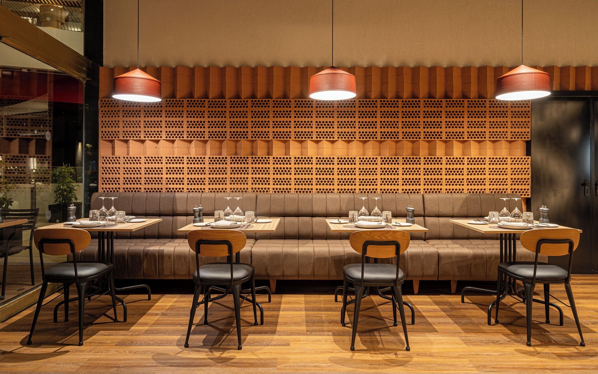 A restaurant with a wooden wall, cushioned seating, and pendant lighting.