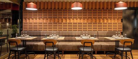 A restaurant with a wooden wall, cushioned seating, and pendant lighting.