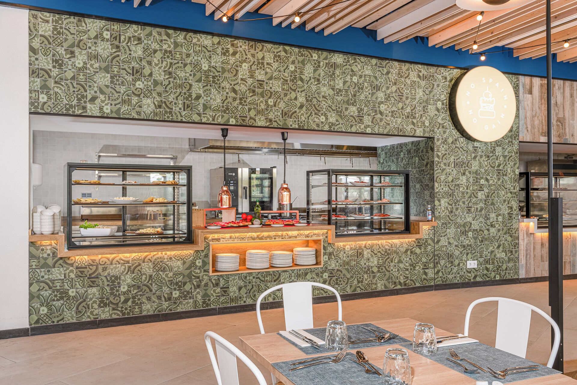 A restaurant with a tiled backsplash, a counter with food displays, and a seating area with tables and chairs.