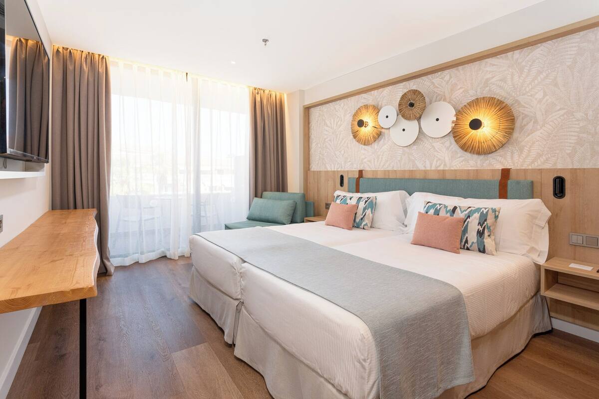 A modern hotel room with a large bed, a wooden desk, and a TV mounted on the wall.