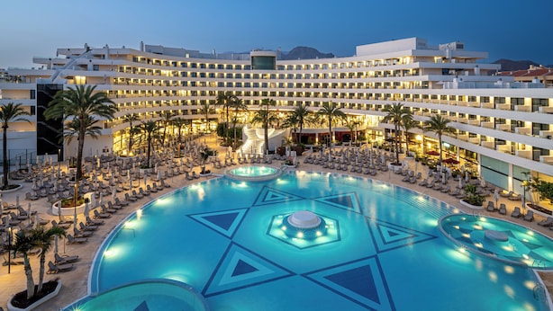 A hotel with a large swimming pool, multiple floors, and a modern design.