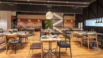 Un restaurante espacioso con varias zonas de comedor, mesas de madera e iluminación moderna.