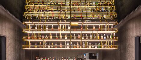 A bar area with multiple shelves of liquor bottles, red bar stools, and a marble countertop.