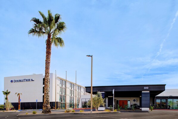 Een DoubleTree hotel met een moderne gevel, palmbomen en een parkeerplaats.