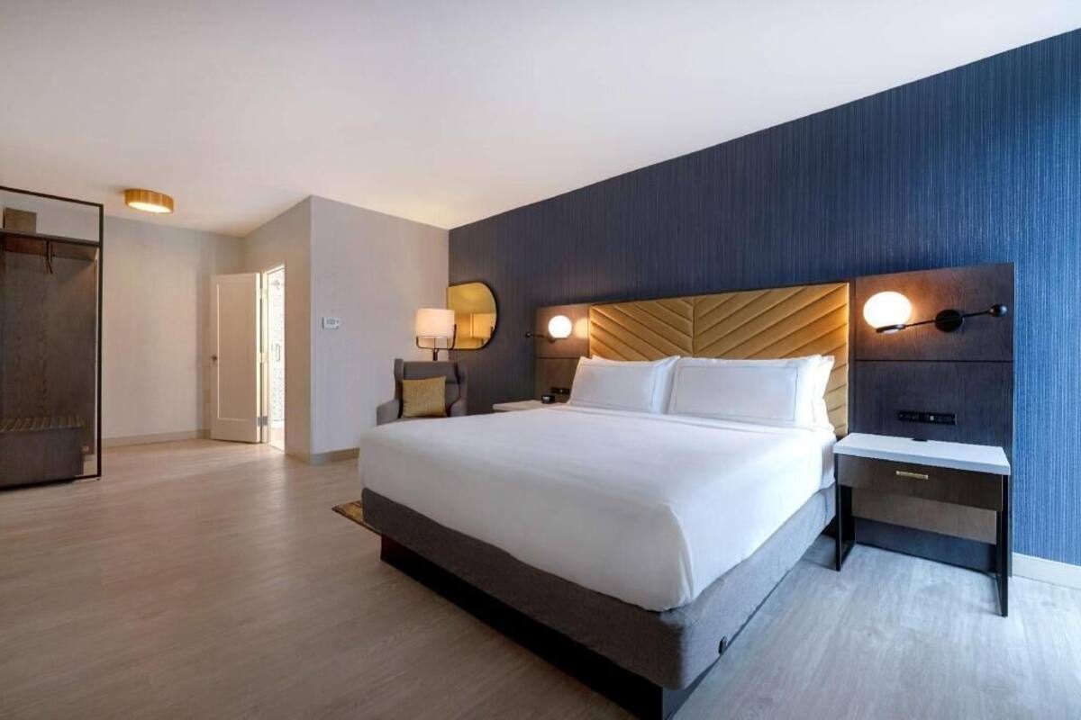 A modern hotel room with a large bed, bedside tables, a wardrobe, and a view of the hallway.